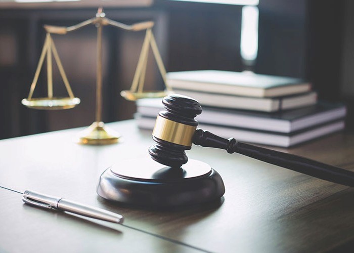 Image of a gavel and gold scales on a desk sat aside a stack of books and a silver pen